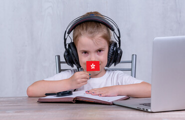 School female child with Hong Kong flag. Child in headphones, with a book and laptop has lesson online