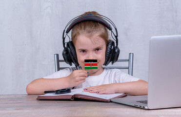 School female child with Kenya flag. Child in headphones, with a book and laptop has lesson online