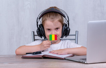 School female child with Mali flag. Child in headphones, with a book and laptop has lesson online