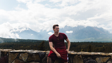 man sitting on a rock fence with mountains in the background