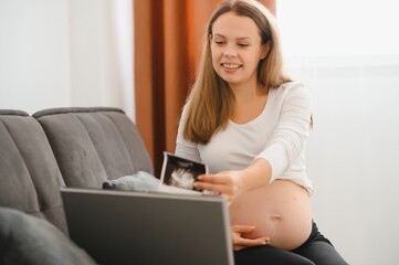 pregnancy, motherhood, people and communication concept - happy pregnant woman with laptop computer having video call and showing ultrasound image at home