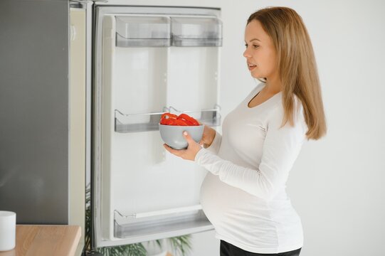 pregnant woman at home in the kitchen opens the refrigerator