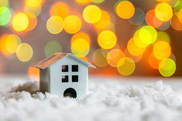 Abstract Advent Christmas Background. Toy model house on snow with defocused garland lights background. Christmas with family at home concept. Christmas winter composition