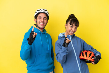 Young cyclist couple isolated on yellow background showing and lifting a finger