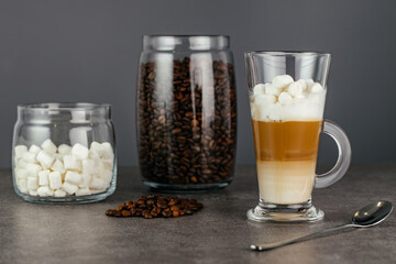 Image of delicious fragrant coffee cappuccino with marshmallows and a jar of coffee beans on a gray...