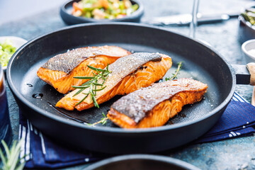 Gebratener Lachs serviert in einer Pfanne mit Beilagen Salat.
