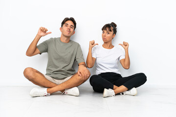 Obraz na płótnie Canvas Young mixed race couple sitting on the floor isolated on white background proud and self-satisfied in love yourself concept