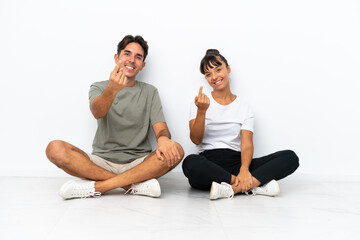 Fototapeta na wymiar Young mixed race couple sitting on the floor isolated on white background shaking hands for closing a good deal