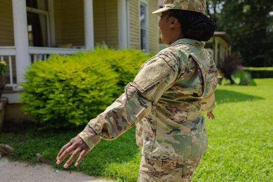 African American Military woman in camouflage uniform walking on front yard with arms outstretched