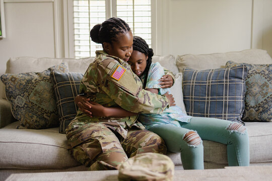 Military woman embracing sad daughter on sofa