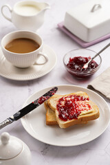 sweet breakfast - toast bread with butter and cherry jam on a white plate, cup of cappuccino