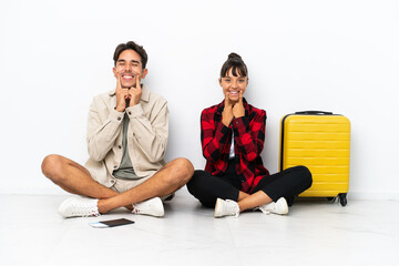 Obraz premium Young mixed race travelers couple sitting on the floor isolated on white background smiling with a happy and pleasant expression