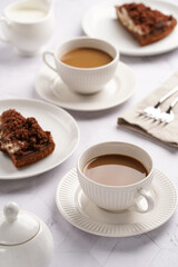 sweet breakfast - two white porcelain cups with coffee drink cappuccino with milk on a white saucer, piece of brown cake