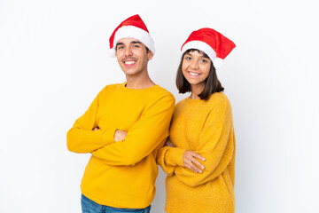 Young mixed race couple celebrating Christmas isolated on white background keeping the arms crossed in lateral position while smiling