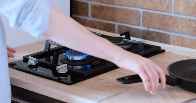 Woman turns on gas stove and puts frying pan on the fire. Girl starts to cook in frying pan. Side view