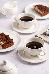 sweet breakfast - two white porcelain cups with coffee drink on a white saucer, piece of brown cake