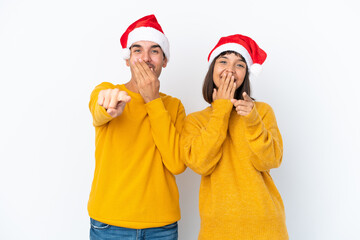 Young mixed race couple celebrating Christmas isolated on white background pointing with finger at someone and laughing