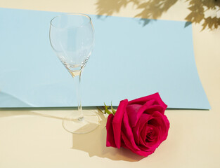 A red rose with an empty wine glass on a blue and beige background. Minimalist concept. Valentine's and anniversary pattern. Love and romance concept.
