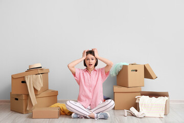 Stressed young woman with wardrobe boxes and things near light wall - obrazy, fototapety, plakaty