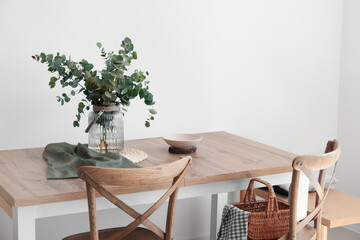 Dining table with eucalyptus branches in vase near light wall - Powered by Adobe