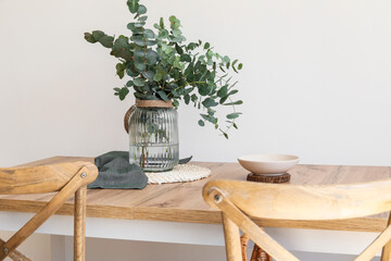 Obraz na płótnie Canvas Dining table with eucalyptus branches in vase near light wall