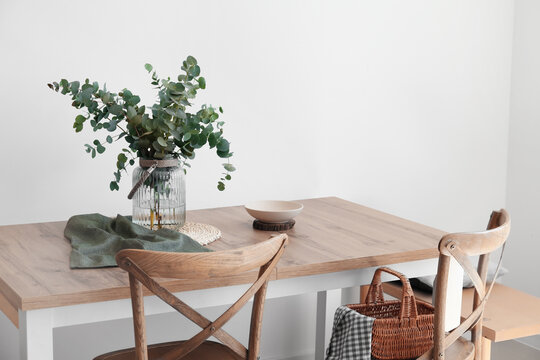 Dining Table With Eucalyptus Branches In Vase Near Light Wall