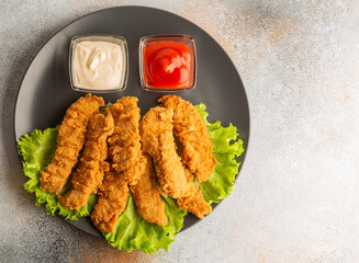 Breaded chicken strips with two kinds of sauces on gray plate. Fast food on gray stone. Flat lay....
