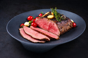 Modern style traditional Commonwealth Sunday roast with sliced cold cuts roast beef with tomatoes and scallions as top view in a design plate