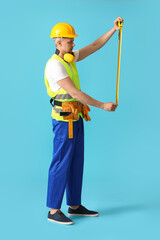 Male builder with tape measure on color background
