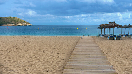 wooden walkway on a sandy beach against the backdrop of the sea, straw umbrellas and plastic sunbeds