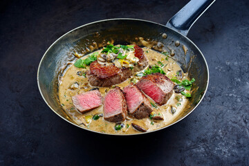 Traditional barbecue dry aged angus roast beef steak natural with mushrooms and onions in cream sauce served as close-up in a classic skillet