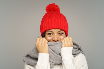 Funny woman in sweater, knitted woolen hat and scarf covering face. Joyful african american female wearing warm clothes for cold weather and frost. Isolated studio portrait of cute cheerful black girl