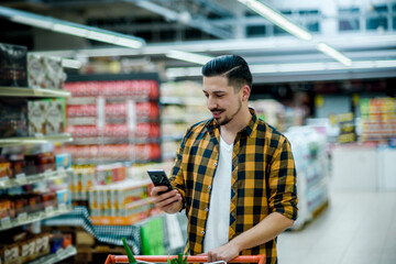 Young handsome man in a supermarket using smartphone while grocery shopping