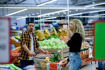 Couple in supermarket using smartphone with shopping cart while grocery shopping