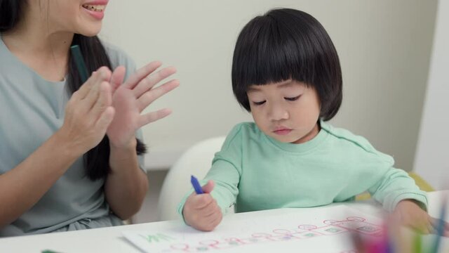 Mom teaching son how to painting with crayon color on book or doing homework. Happy asian boy painting with crayon and colored pencil with his mother in living room at home.  family concept.