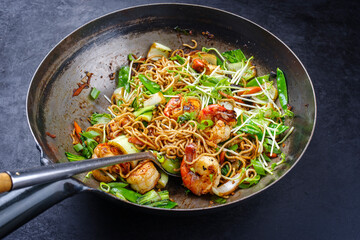Traditional stir-fried Thai phak kung with king prawns, vegetable and noodles served as close-up in a classic design wok