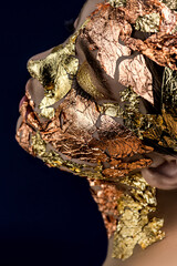 Close-up of beautiful young woman's face with golden makeup imitated luxury mask on half of her face and natural makeup on other half, selective focus on eye. SPA skin care and wellness concept
