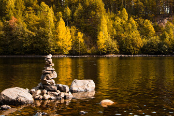Beautiful landscape. Pyramid made by stones. Stone tower and river, forest in the background. Rocks on the pine forest. Stone pile was made by tourist. Concept of balance, harmony and vacation.