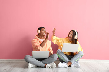 Stylish young couple in hoodies giving each other high-five near pink wall