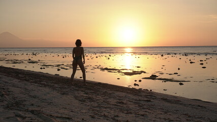 Naklejka premium Girl walking on the beach at sunset island Indonesia travel Bali Gili T summer sun golden hour coast ocean relax nature adventure woman
