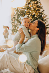 Mother with her baby daughter sitting by the Christmas tree