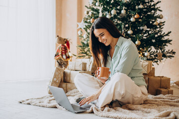 Woman on Christmas using laptop and drinking tea by the Christmas tree