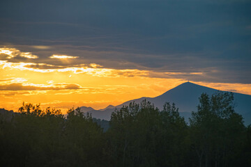 Beautiful view of a mountain range and trees under a cloudy sky at sunset