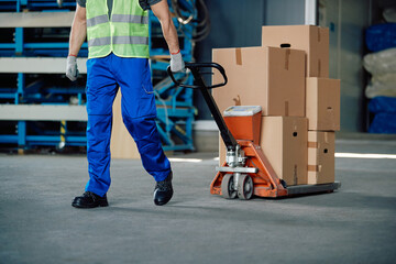Unrecognizable worker pulls pallet jack while working at distribution warehouse.