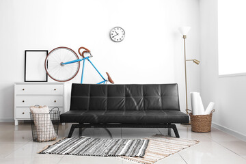 Interior of light living room with black sofa, chest of drawers and bicycle