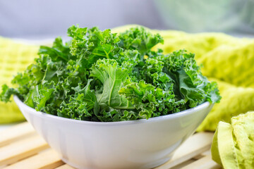 Fresh green curly cabbage or kale salad leaves cut in the bowl on light background on the table in the kitchen.