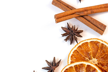 Top view flat lay of Christmas spices for traditional beverages: cinnamon sticks, anise stars, dry orange slices as a frame for Xmas seasonal decorations on white background with copy space.
