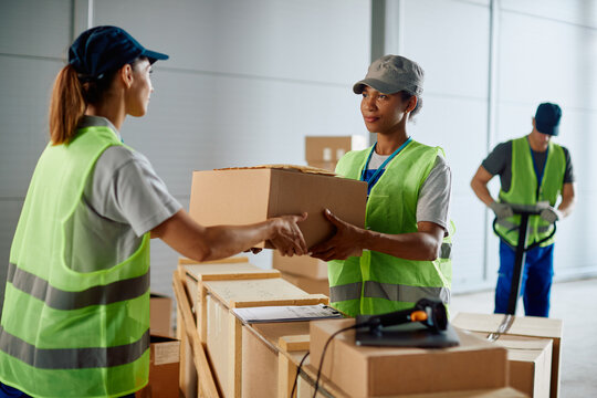 Female workers cooperate while working with cardboard shipping boxes at distribution warehouse.