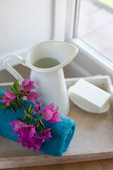 A white jug of water, a towel and soap are on a tray on a wooden table by the window. The theme is morning hygiene procedures. Retro style. Vertical image.
