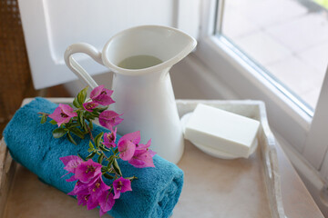 A white jug of water, a turquoise towel and soap are on a tray on a wooden table by the window. The theme is morning hygiene procedures. Retro style.